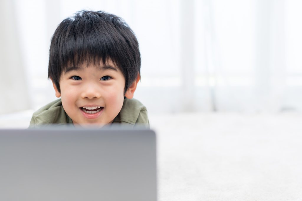 パソコンを操作しながら笑顔でこちらをみている男の子